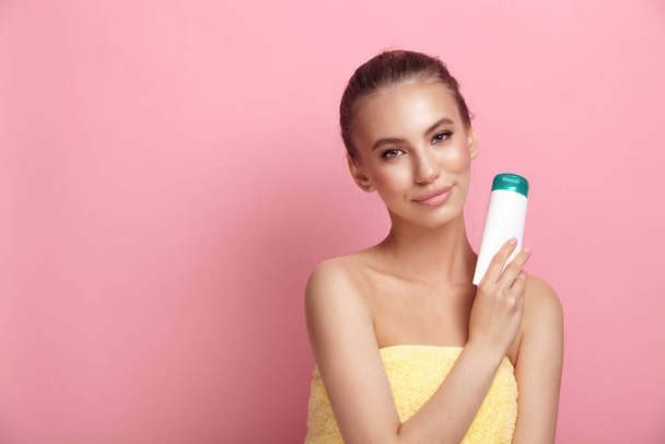 Female model holds plastic tube of lotion on pink background - Фото, зображення