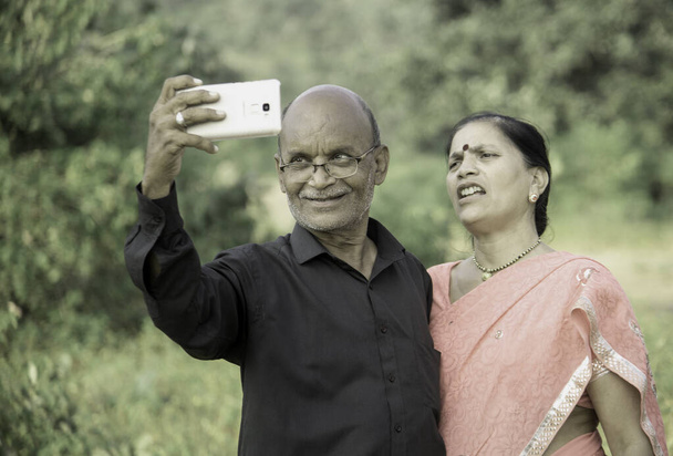 Ευτυχισμένο ζευγάρι ηλικιωμένων Ινδών που χρησιμοποιούν smartphone, κοιτάζοντας φωτογραφίες στο smartphone. - Φωτογραφία, εικόνα