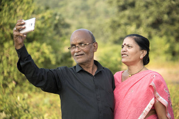 Glückliches älteres indisches Paar macht ein Selfie auf dem Smartphone und lächelt gemeinsam im Freien.  - Foto, Bild