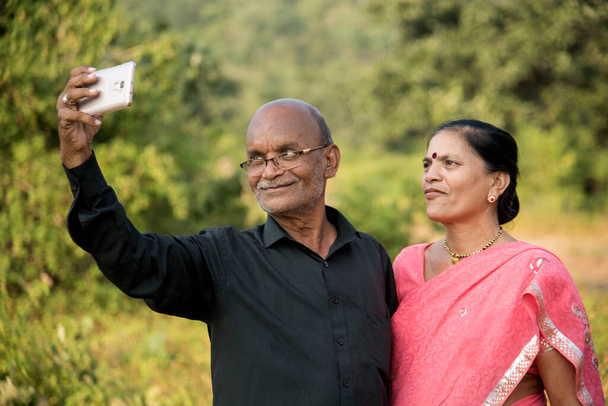 スマートフォンで写真を見る幸せなシニアインド人カップル. - 写真・画像