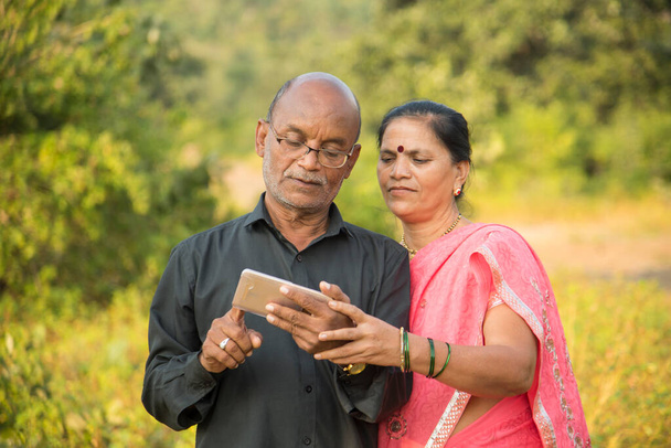 Happy senior Indian couple using smartphone, looking at  photos on smartphone. - Photo, Image