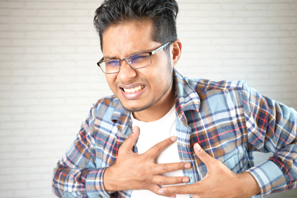 junger Mann erleidet Schmerzen im Herzen und hält Brust mit der Hand  - Foto, Bild