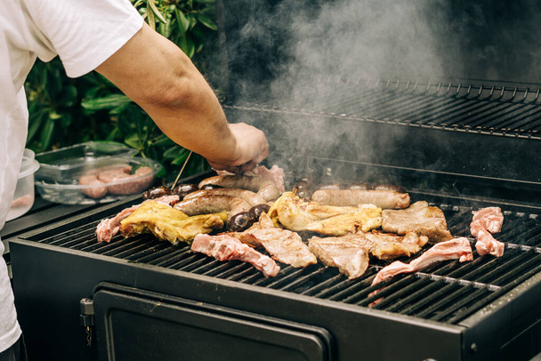 человек гриль мясо на барбекю различные виды мяса, курица, колбасы, кровяная колбаса, ягненок на гриле в саду - Фото, изображение