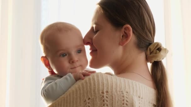 Portret małego dziecka i uśmiechnięta matka przytulająca się w domu. Pojęcie szczęścia rodzinnego i rodzicielstwa - Materiał filmowy, wideo