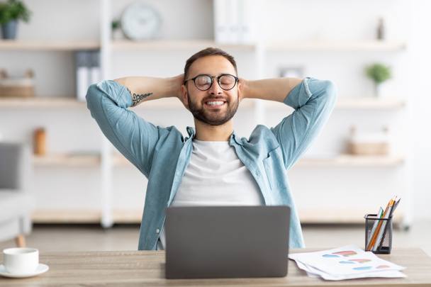 Χαμογελώντας Καυκάσιος επιχειρηματίας έχει ξεκουραστεί μπροστά από το φορητό υπολογιστή στο γραφείο στο σπίτι, λαμβάνοντας διάλειμμα από την online δουλειά - Φωτογραφία, εικόνα