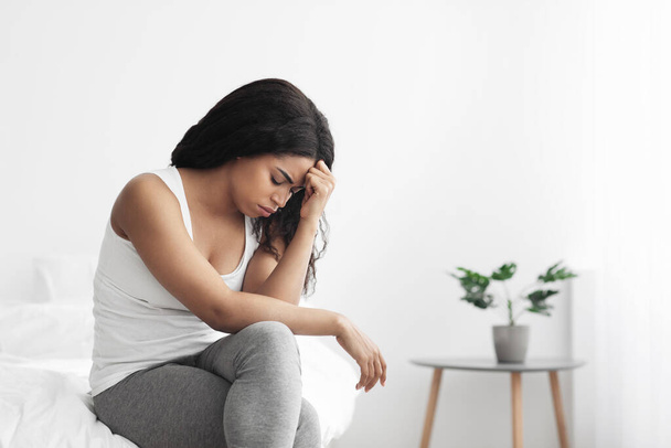 Dama afro-americana estressada pensando no problema ou tendo depressão, segurando a cabeça, sentada na cama, espaço livre - Foto, Imagem