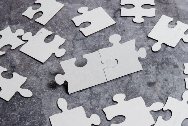 Close-Up White Jigsaw Pattern Puzzle Pieces To Be Connected With Missing Last Piece Positioned On A Flat Lay Background With Different Texture And Paper Supplies Accesories - Photo, Image