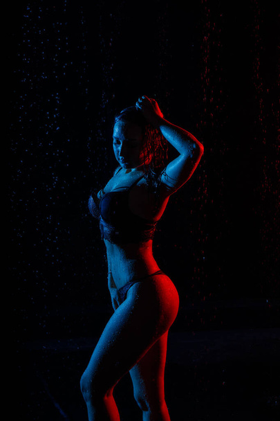 Mujer en la camisa blanca con gota de agua en una habitación oscura iluminada por la luz con agua - Foto, imagen