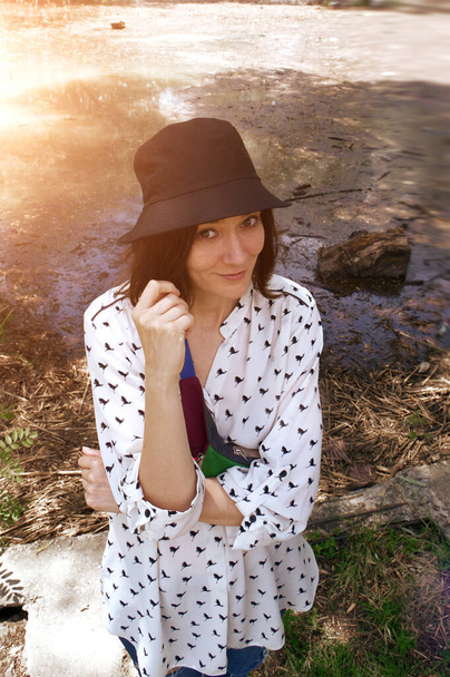 Brown-haired girl in a hat smiling. pond in the forest in the background - Photo, Image