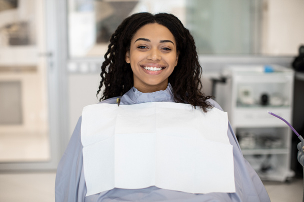 Портрет счастливой чёрной пациентки, сидящей в кресле в стоматологической клинике - Фото, изображение