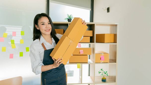 Азійська молода жінка SME діловий власник з онлайн-магазинами працює на ноутбуці з посилкою коробки на столі - SME онлайн бізнес ідея і доставка - Фото, зображення