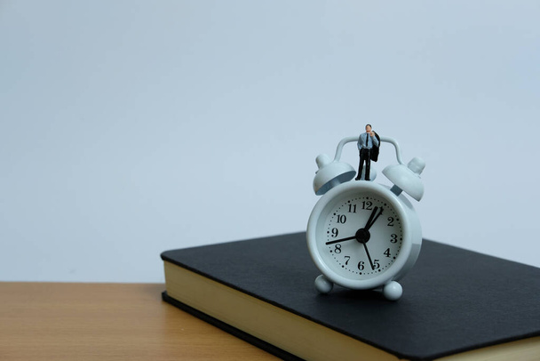 Minyatür iş kavramı. Saatin ve defterin üzerinde duran bir adam. iş yükü kavramı - Fotoğraf, Görsel