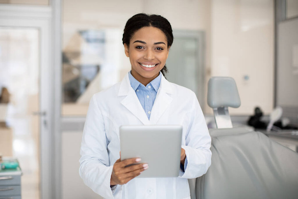 Lächelnde schwarze Zahnärztin mit digitalem Tablet posiert in Klinik für Stomatologie - Foto, Bild