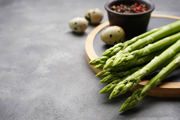 Green fresh asparagus and kitchen board on gray background, space for text. - Foto, afbeelding