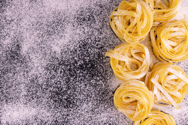 Fresh Italian tagliatelle pasta sprinkled with flour on a black background. Copy space. - Zdjęcie, obraz