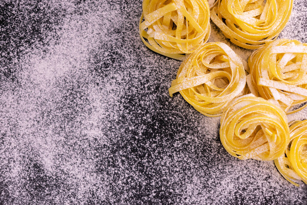Fresh Italian tagliatelle pasta sprinkled with flour on a black background. Copy space. - Foto, Bild