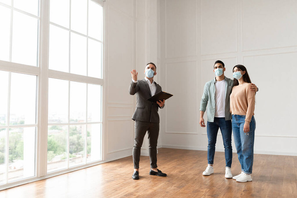 Agente imobiliário em máscara médica mostrando compradores novo apartamento - Foto, Imagem