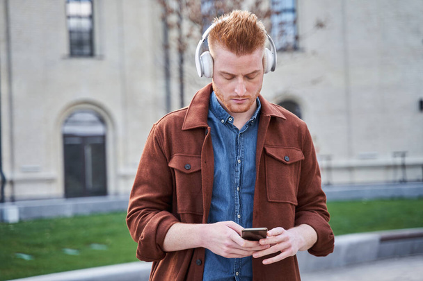 Man looking at the smartphone and listening music while standing - Photo, image