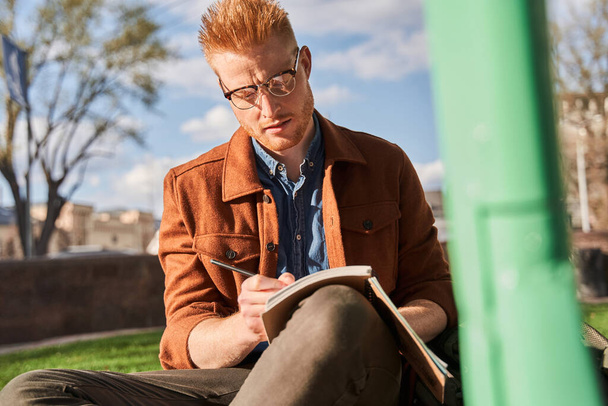 Man wearing glasses writing into notebook while spending time at the nature - Photo, image
