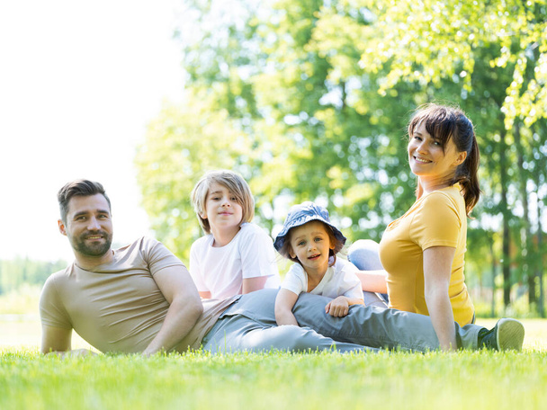 Portrait of happy family of parents and two children sitting in park outdoors and smiling - Foto, afbeelding
