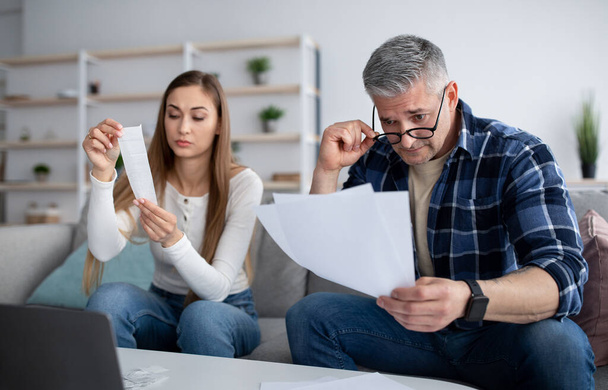 Gezinsplanning. Getrouwd volwassen paar met documenten en rekeningen tellen hun financiën op laptop thuis - Foto, afbeelding