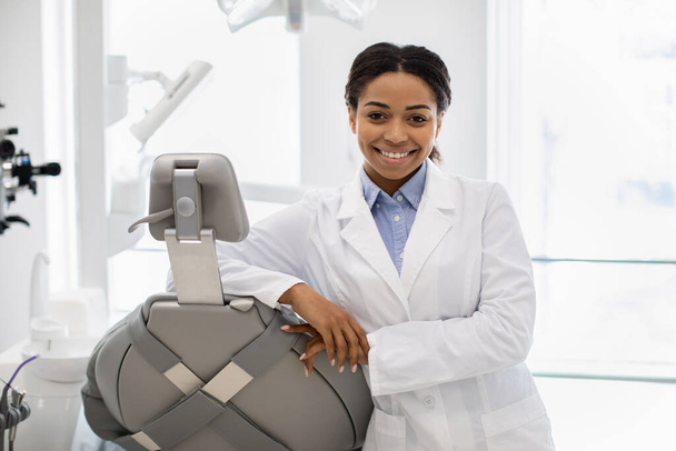 Professionele zwarte vrouwelijke stomatoloog arts poseren op de werkplek in moderne kliniek - Foto, afbeelding