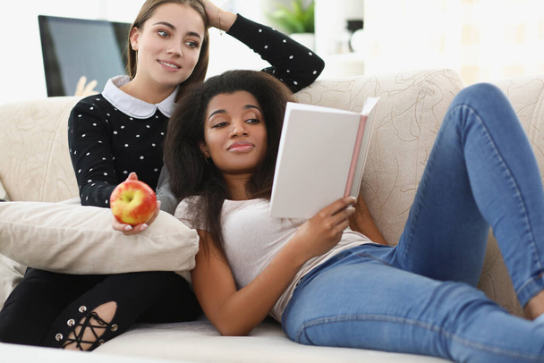 Mulheres caucasianas e afro-americanas leem planejador diário no sofá - Foto, Imagem