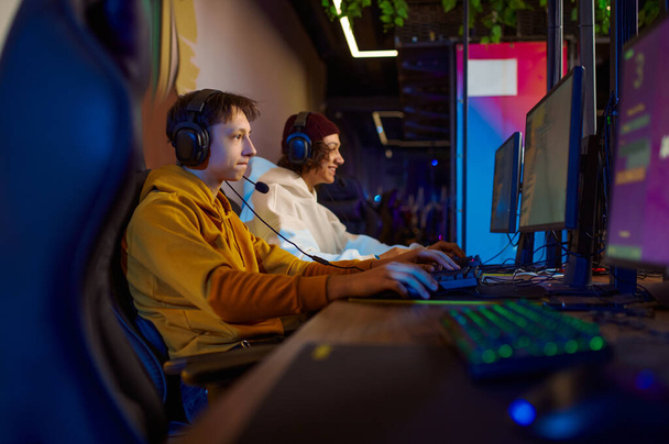 Two young gamers in headsets play in video game club - Foto, afbeelding