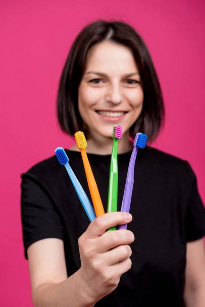 Beautiful happy young woman with different colored toothbrushes on blank pink background - Photo, image
