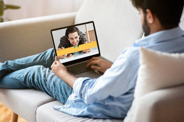 Młodzieniec oglądający samouczek wideo DIY na laptopie, uczący się naprawiać lub odnawiać swój dom, korzystający z nowoczesnych technologii - Zdjęcie, obraz