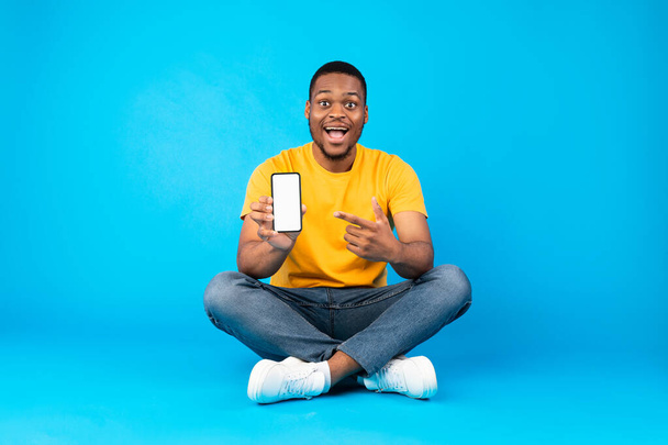 Opgewonden zwarte man toont smartphone leeg scherm over blauwe achtergrond - Foto, afbeelding