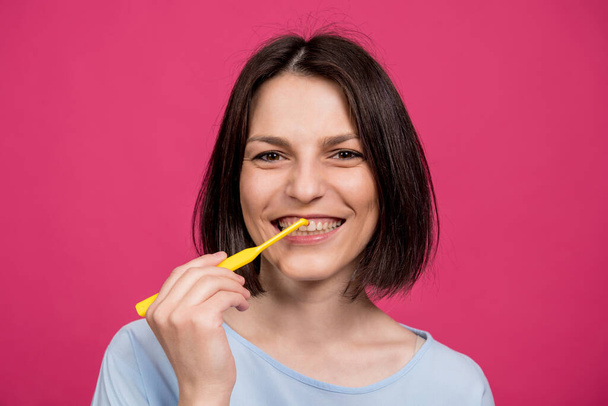 Beautiful happy young woman with single tufted toothbrush on blank pink background - Фото, зображення
