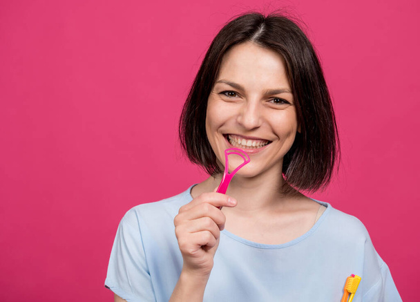 Beautiful happy young woman with tongue scraper on blank pink background - Zdjęcie, obraz
