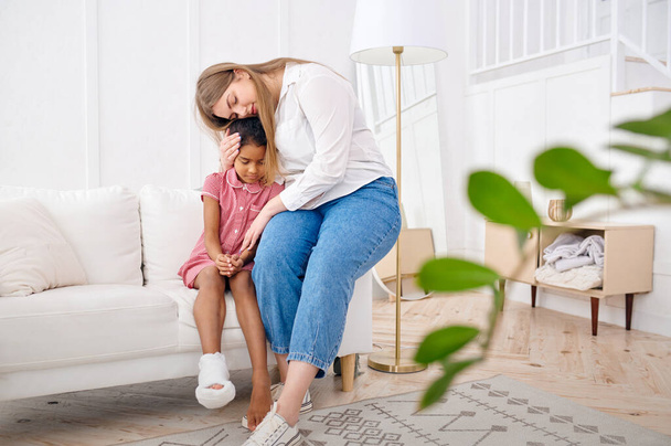 Mother feels sorry for her little daughter on sofa in living room.Mom and female child leisure in their house together, good relationship, parental care and love - Φωτογραφία, εικόνα
