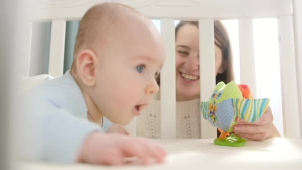 A kisbaba bölcsőben mászkál és színes játékokért nyúl. A szülőség, a család boldogsága és a baba fejlődése - Felvétel, videó