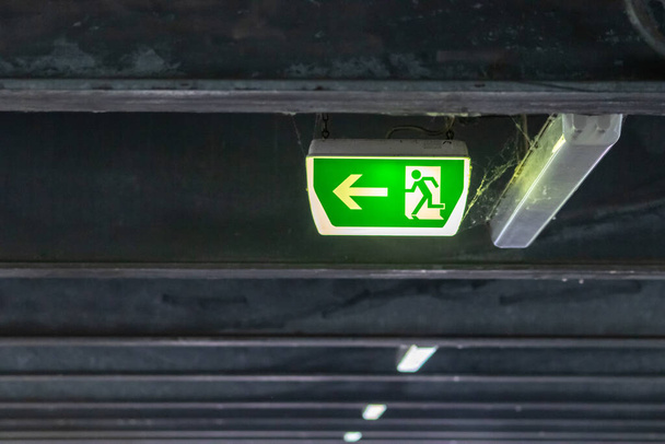 走行者と緑の矢印と緑の出口標識は、天井で危険な状況での救助と避難の安全のための駐車場での誘導システムの標識を示しています極端な危険の生活を救出 - 写真・画像