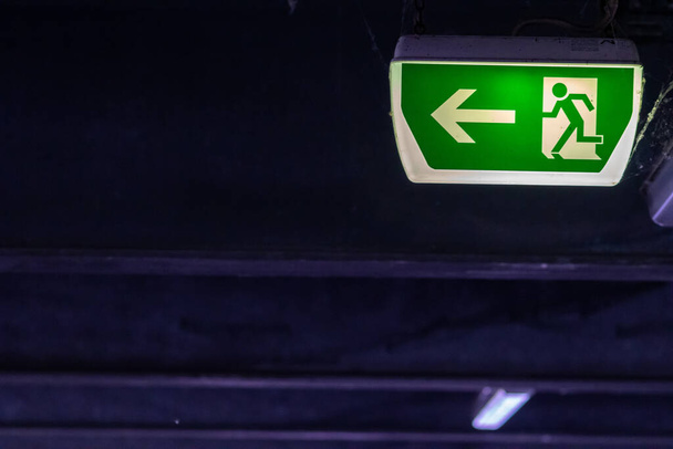 走行者と緑の矢印と緑の出口標識は、天井で危険な状況での救助と避難の安全のための駐車場での誘導システムの標識を示しています極端な危険の生活を救出 - 写真・画像