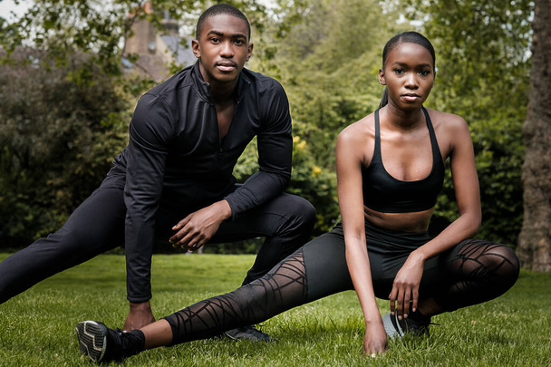 Black brother and sister twins doing exercise outdoors in stylish sportswear. They are in a park in a cloudy spring day. - Photo, Image