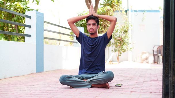 Ινδός νεαρός διαλογίζεται στο σπίτι. Πορτρέτο της Ασίας χαριτωμένο αγόρι πρακτική γιόγκα στο σπίτι φόντο. Παγκόσμια ημέρα γιόγκα έννοια. - Φωτογραφία, εικόνα