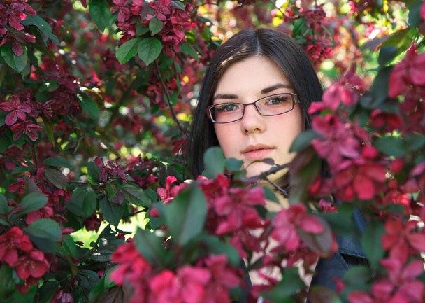 portrait of young beautiful brunette girl in black jacket and burgundy sweater standing near cherry blossoms on sunny spring day. outdoor closeup - Φωτογραφία, εικόνα