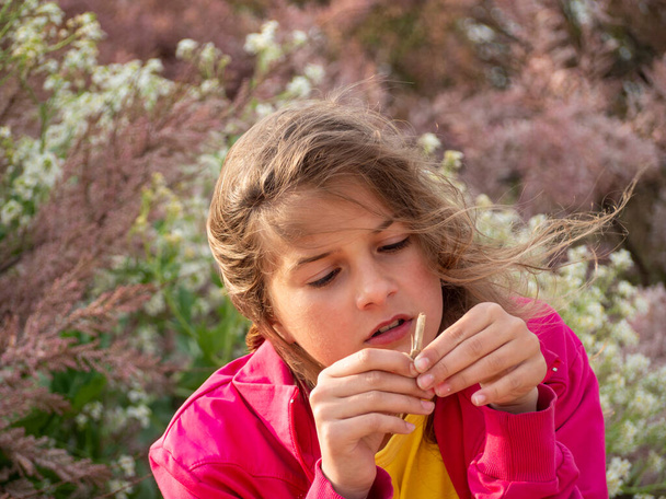 Egy aranyos tinédzser lány figyelmesen vizsgál egy fa botot, miközben egy tavaszi virágzó kertben van. Egy gyönyörű lány egy ágat tart a kezében. Valódi élet, természetes fény.. - Fotó, kép
