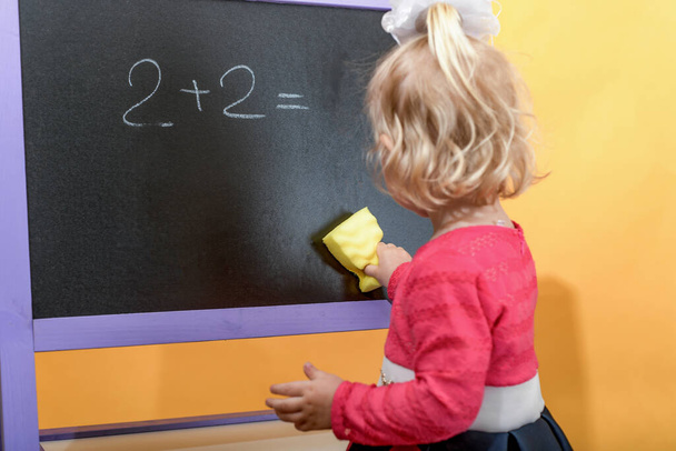 The child wipes the blackboard with a damp sponge from inscriptions and drawings. The concept of preschool education for children. - Photo, Image
