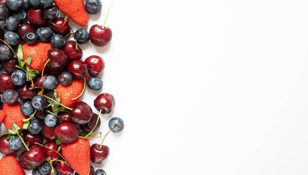 lots of strawberries, cherries and blueberries. juicy summer on white background with copy space. - Photo, image