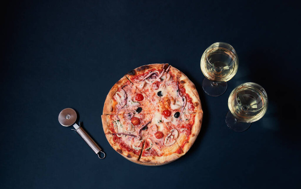 Delicious seafood pizza, pizza cutter and glasses of white wine on dark background. Top view, copy space. - Fotó, kép