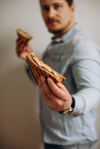 sandwich in male hands on a white background. half of the sandwich in the hands of the man. guy karate holds a sandwich. - Zdjęcie, obraz
