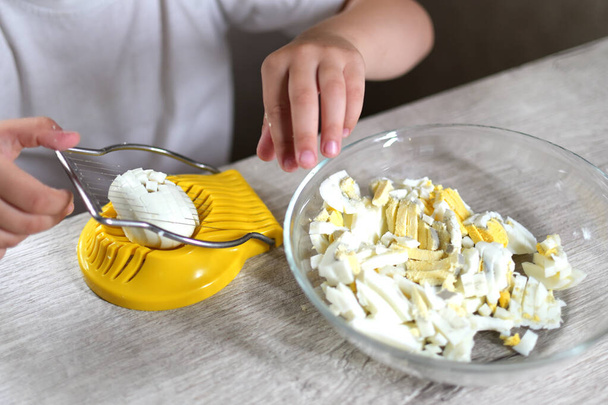 τρόπο ζωής προσχολικής κορίτσι παιδί μαγειρεύουν τα τρόφιμα στην κουζίνα. ανάπτυξη καλών κινητικών δεξιοτήτων στην καθημερινή ζωή από άχρηστα υλικά. το παιδί κόβει τα αυγά με ένα κίτρινο κόφτη αυγών - Φωτογραφία, εικόνα