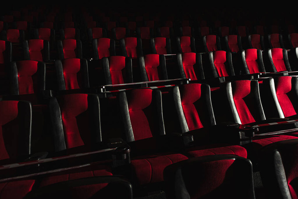 Empty movie theater. Armchairs red and black in the cinema hall are illuminated by a beam of light, low key. Selective focus. Quarantine, restrictive tape on chairs - Photo, Image