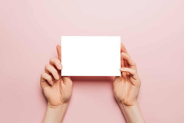 Female hands hold a blank sheet of paper on a pink background. Advertising space - Фото, зображення