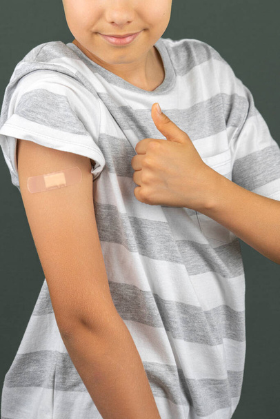 Χαμογελαστός έφηβος που δείχνει στο χέρι του με γύψο μετά τον εμβολιασμό. Εμβόλιο και υγειονομική περίθαλψη κατά τη διάρκεια πανδημίας covid-19 - Φωτογραφία, εικόνα