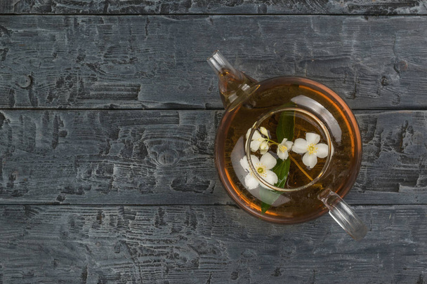 Bovenaanzicht van een glazen theepot met jasmijnthee op een zwarte houten tafel. Een verkwikkende drank die goed is voor je gezondheid. - Foto, afbeelding